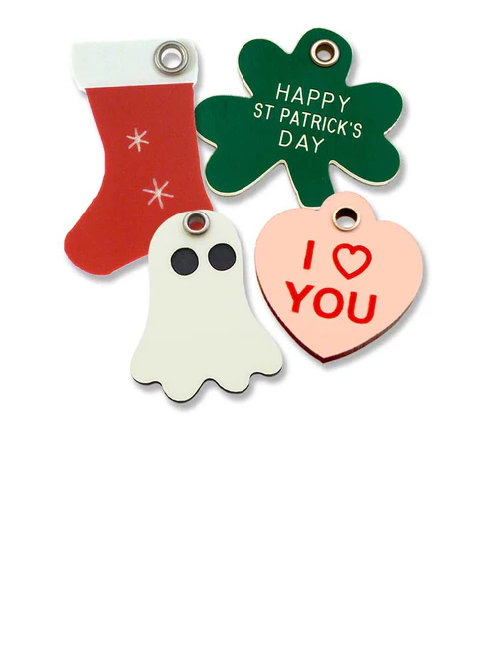 A red holiday stocking shaped plastic tag, a green shamrock shaped stocking tag, an off-white ghost shaped tag and a pink heart stamped with "I Heart You".